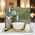 Set of tea-making tools including a bowl, whisk, and other accessories with a green box in the background.